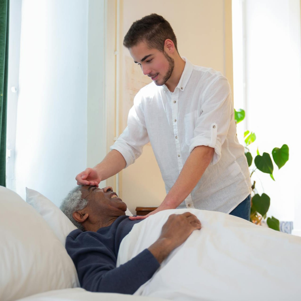 Ein junger Pfleger fühlt die Stirn eines älteren Mann.
